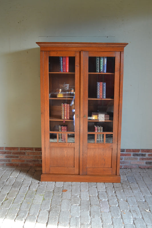Antieke eiken houten Art Deco boekenkast met beglaasde deuren. Achter de twee deuren in hoogte verstelbare planken. Antieke winkelkast, antiek vitrinekast, antieke servieskast, antieke bibliotheekkast. antieke kantoorkast, antieke opbergkast, antieke Hollandse kast, antieke woonkamerkast, antieke keukenkast.
